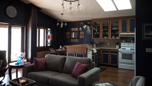 A spacious living room with a gray sofa, wooden cabinets, and a kitchen area with wooden cabinets and white appliances. - Plaza Perch~Downtown~Walkable (Arcata)