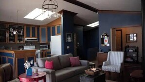 A living room with a sofa, armchair, and a small table with a vase. There is a kitchen area with cabinets and a microwave. - Plaza Perch~Downtown~Walkable (Arcata)