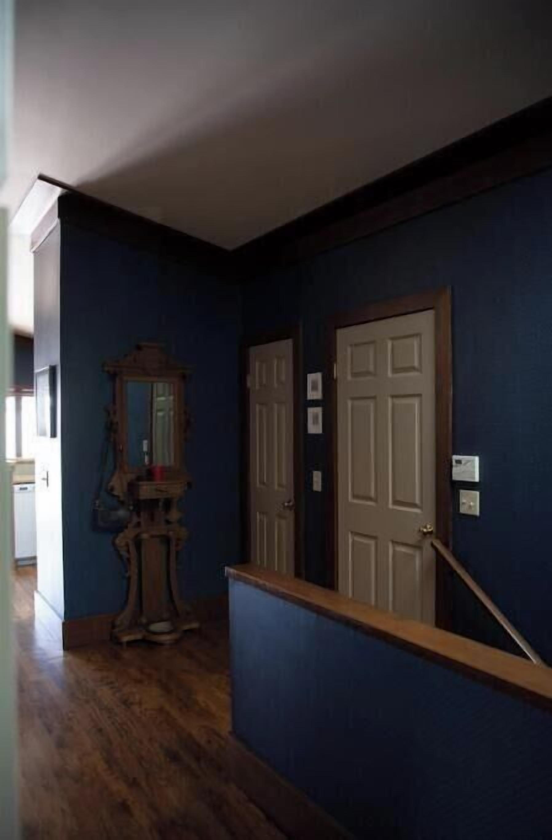 A hallway with wooden flooring, a blue wall, and a door with a white frame.