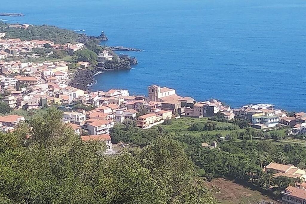 Una località costiera con edifici lungo la riva, una chiesa importante e un promontorio roccioso in lontananza.