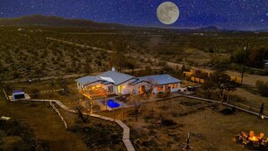 Une maison avec une piscine, une cour clôturée et une grande lune dans le ciel.