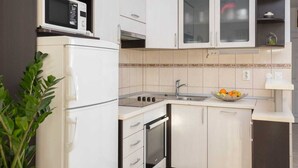 A compact kitchen with white cabinets, a microwave, a stove, and a sink. - Lavica seaside apartments (Podstrana)
