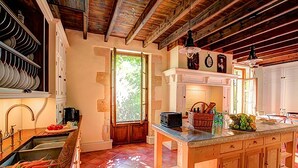 A rustic kitchen with wooden beams, a large island, and a window with a view of greenery. - Beautiful Stone Farmhouse, Private Pool, Idyllic Setting Amongst Vineyards near Sainte-Foy-la-Grande (Sainte Foy la Grande)