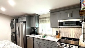 Una cocina moderna con armarios grises, electrodomésticos de acero inoxidable, encimera de granito y piso de madera.