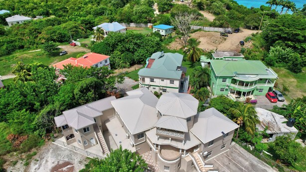 Une grande maison à plusieurs étages, dotée d’une cour intérieure, entourée d’une végétation luxuriante et donnant sur une plage.
