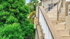 Un escalier aux marches de couleur beige et aux rampes blanches, menant à un bâtiment dont la façade présente une texture particulière.