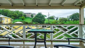 Un espace extérieur abrité, doté d’une table et de chaises, qui offre une vue sur un quartier résidentiel avec ses maisons et sa verdure.