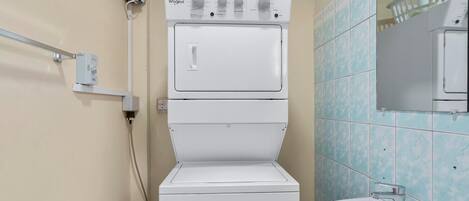 A compact, two-tiered washer-dryer unit in a bathroom with light blue tiles and a beige wall.