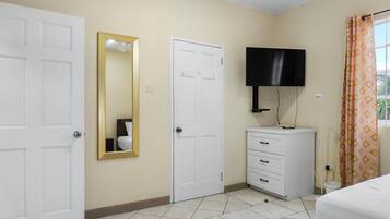 A bedroom with two white doors, a white dresser, a flat-screen TV mounted above it, and a bed with a white bedspread.