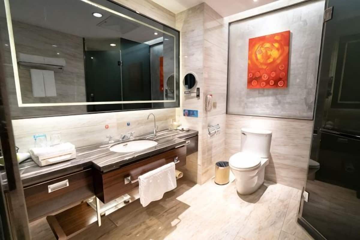 Une salle de bain moderne avec un grand miroir, deux vasques, des toilettes et une poubelle.