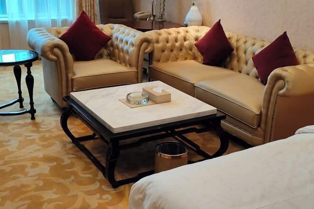 Quarto de hotel com sofá estofado, uma mesa redonda pequena, uma mesa de centro retangular e uma cama.