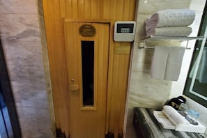 A wooden sauna door with a plaque, a control panel, towels, and a small table with a bottle and glass. - Gold Harbour Holiday Hotel (Jiexiu)