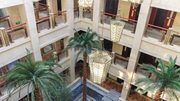 Un atrium à plusieurs niveaux, agrémenté de palmiers, d’un sol à motifs et de lanternes suspendues.
