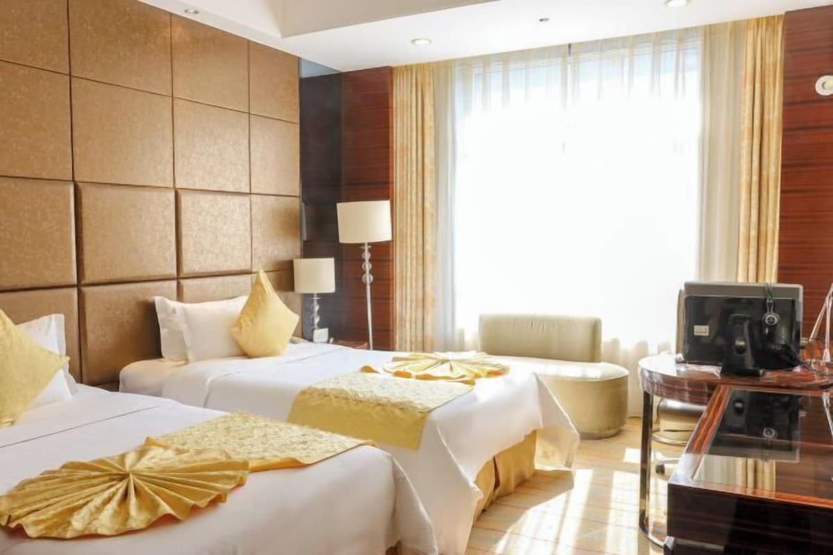 A hotel room with two beds, a desk, a chair, and a TV.