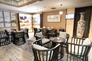 A restaurant with round tables and chairs, a large vase, and framed artwork on the walls.