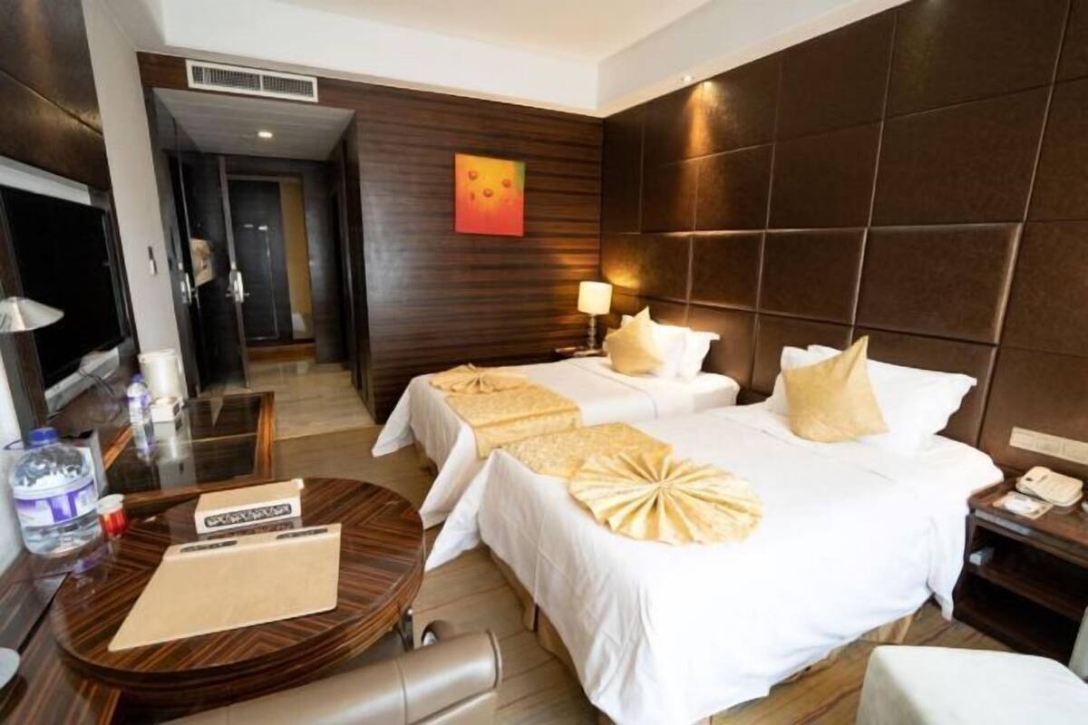 Une chambre d’hôtel avec deux lits, une table ronde en bois, une table de chevet avec une lampe et un tableau au mur.
