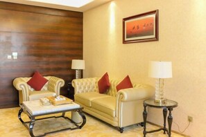 A room with a beige sofa, a matching armchair, a small table, and a lamp. - Gold Harbour Holiday Hotel (Jiexiu)