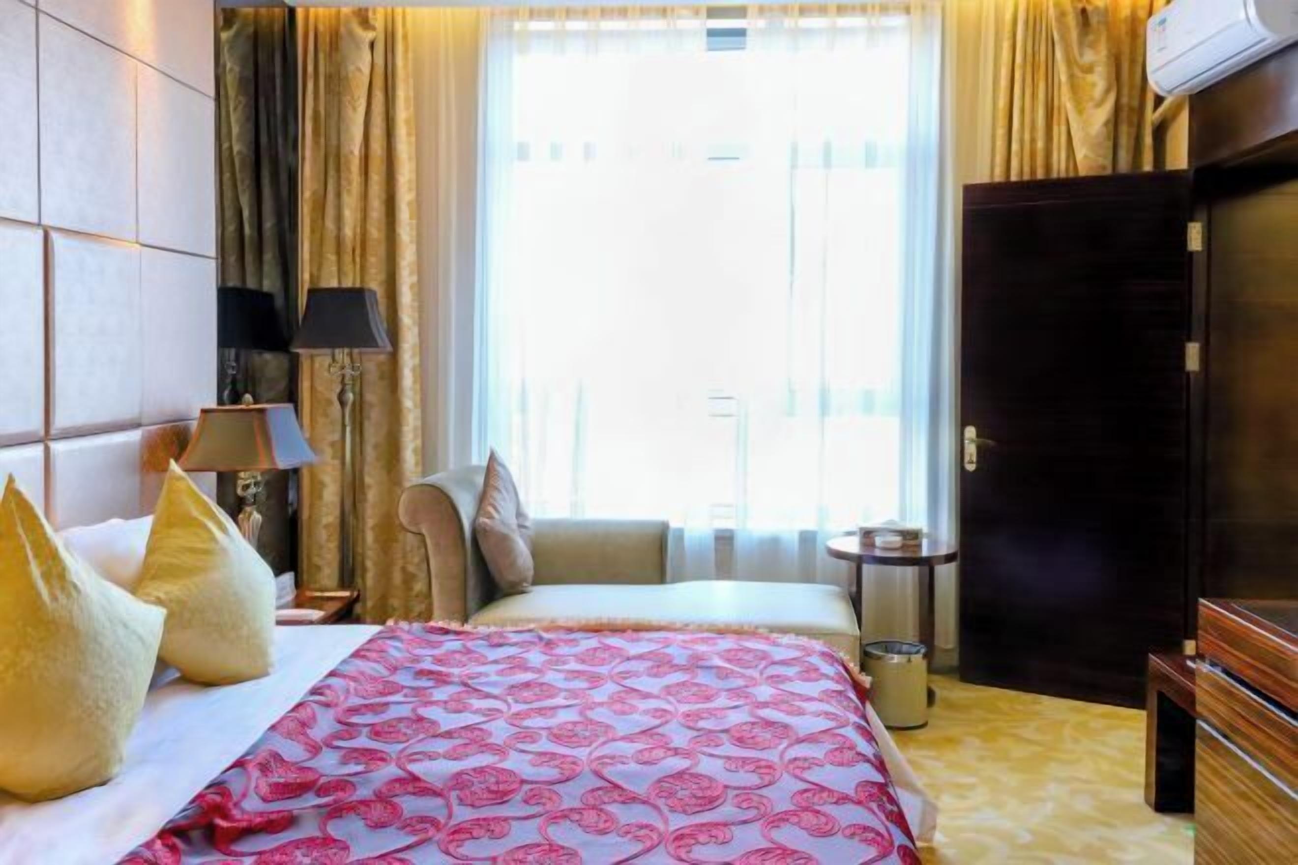 Habitación de hotel con cama, mesita de noche con lámparas, armario y ventana con cortinas.