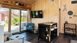 Een gezellig cabin interieur met houten plafond, een aan de muur bevestigde televisie, een blauwe stoel, een klein tafeltje en een schuifdeur van glas die leidt naar een buitenruimte.