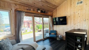 Een gezellig interieur van een blokhut met een bank, een klein rond tafeltje, een televisie en een houten plafond met dakramen.