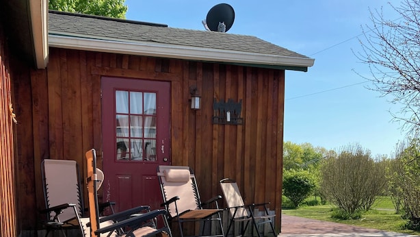 En stuga av trä med en röd dörr, en satellantenn och en veranda med fyra solstolar.