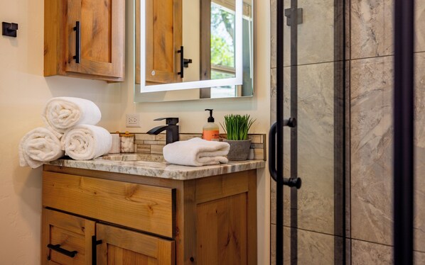A bathroom with wooden cabinets, a marble countertop, a sink with a faucet, a mirror, and a potted plant.