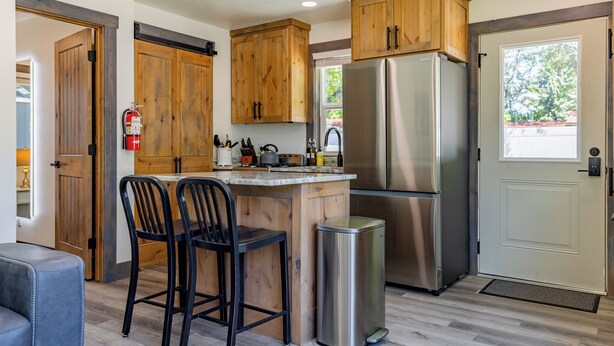 A modern kitchen with wooden cabinets, a stainless steel refrigerator, and a small trash bin. - Beautiful NEW 1-bed, 1-bath right in downtown Cody! Sleeps up to 4.  (Cody)