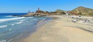 A beach with a lighthouse, sandy shore, and buildings in the background.