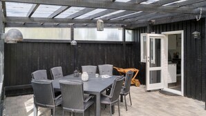 A covered patio area with a table and chairs, a lantern, and a door leading to an interior space.