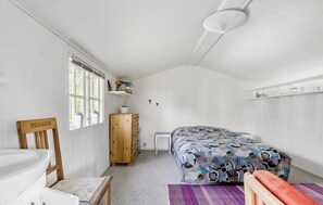 Et soveværelse med en seng, et træskab, en stol, et lille bord og et vindue med gardiner.