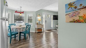 A dining area with teal chairs, a table with a floral tablecloth, and a wall-mounted sign that reads "beach". - 1802A Ocean Lakes Pet Friendly Golf Cart⛱️🏝️🩱🌊👙☀️🐚 (Myrtle Beach)