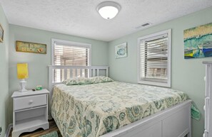 Un dormitorio con cama, mesita de noche, lámpara y ventana con persianas.