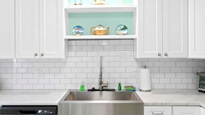 Una cocina con armarios blancos, un lavamanos de acero inoxidable y un salpicadero de azulejos.