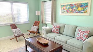 Un salón con pared verde claro, un sofá color beige, dos sillones estampados, una mesa de centro de madera y un cuadro de colores.