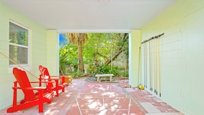 Un patio techado con sillas Adirondack rojas, un banco y una cancha de tenis.