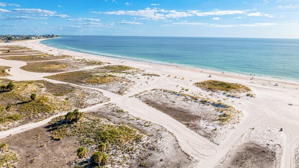 Un paisaje costero con una playa arenosa, cielo azul despejado y una línea de costa distante.