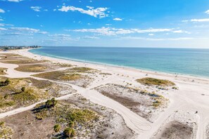 Un paysage côtier avec une plage de sable, un ciel bleu dégagé et une ligne de côte lointaine.