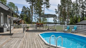 Eine Holzterrasse mit Pool, Sitzgelegenheit und Blick auf hohe Bäume.