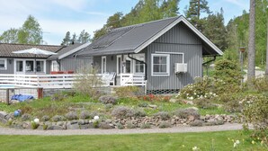 Eine zweistöckige Holzhütte mit Veranda, umgeben von einem Garten mit verschiedenen Pflanzen und Blumen.
