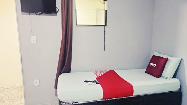 A single bed with a red blanket and a pillow with the word "oyo" on it. There is a television mounted on the wall to the left of the bed. - Hotel Ita Avenida (Itaborai)