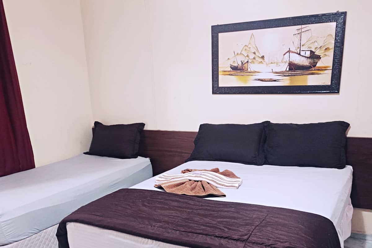 A double bed with a brown blanket and pillows, a single bed with a white sheet, and a painting of a boat on the wall.