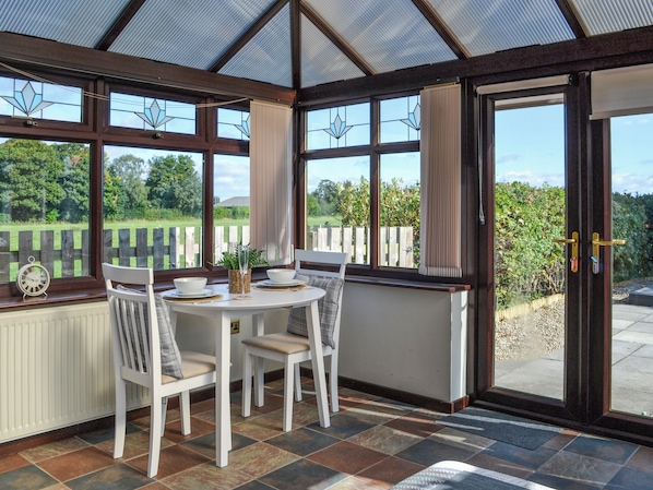 A conservatory with a table and chairs, large windows, and a view of the outdoors.