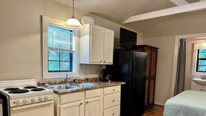 A compact kitchen with white cabinets, a black refrigerator, a stove, and a sink. - Meadows - A tiny touch of heaven at Stag Leap Cabins! (Nacogdoches)