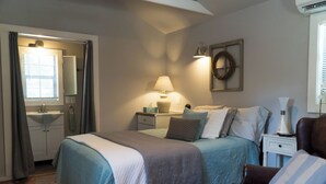 A bedroom with a bed, bedside tables, a lamp, a mirror, a window with curtains, and a wall-mounted wreath. - Meadows - A tiny touch of heaven at Stag Leap Cabins! (Nacogdoches)
