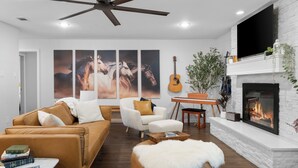 Een moderne woonkamer met een bank, fauteuil en voetenbankje, een open haard en een aan de muur bevestigde gitaar.