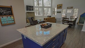 A spacious living area with a large island, a fireplace, and a view of the outdoors through large windows. - OASIS IN THE FOREST ON 1.25 ACRE BACKING TO NATIONAL FOREST WITH AC-PETS WELCOME (Show Low)