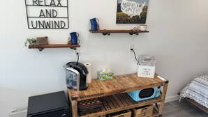 Een gezellige kamer met een koffiezetapparaat, een plank met mokken, een lijst met een foto en een houten opbergmeubel met gelabelde lades.