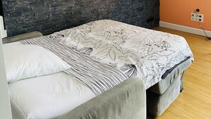 Un dormitorio con cabecera de piedra, una cama con ropa de cama estampada y tres cuadros colgados en la pared.