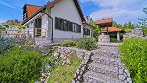 A house with a stone pathway leading to a patio area, surrounded by greenery and a stone wall. - Beautiful home in Donji Zvecaj with WiFi (Donji Zvecaj)