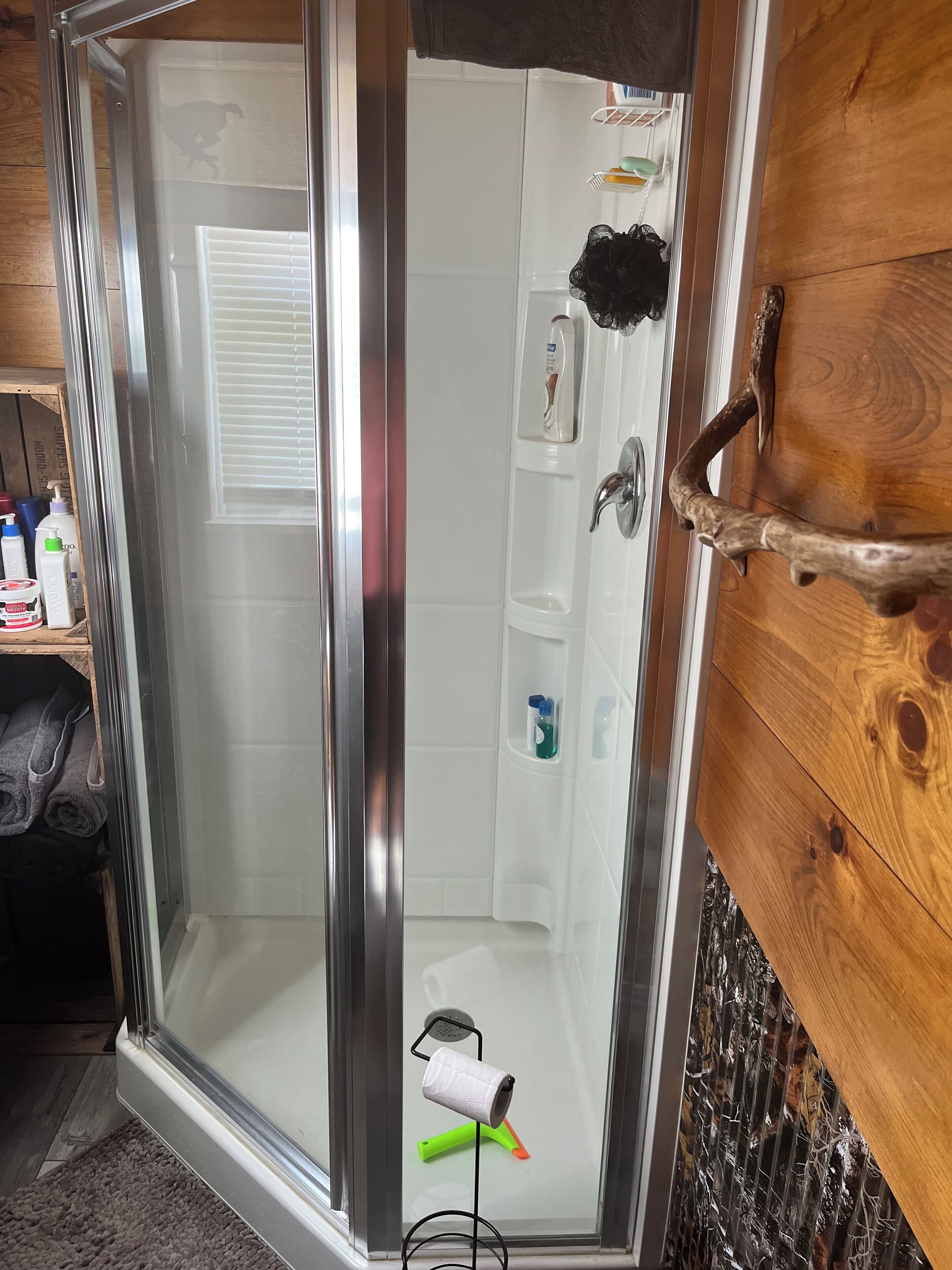 A glass-enclosed shower with a wooden wall, a towel rack, and a shelf with toiletries.